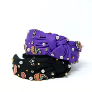 Two knotted fabric headbands stacked on a white background, one in purple and one in black, both decorated with small pumpkin charms, white faux pearls, and gold and silver rhinestones.